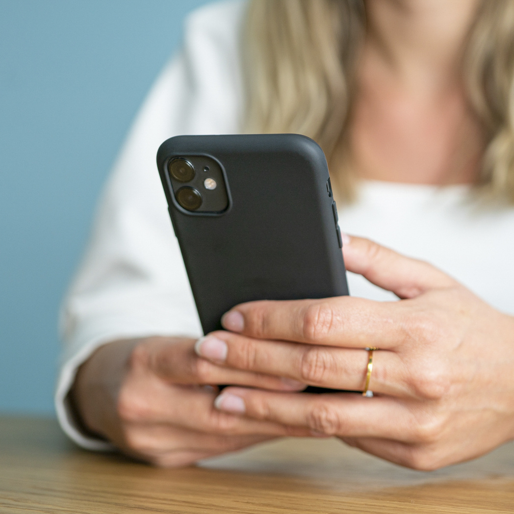 Una persona che tiene in mano un telefono nero, con un anello d'oro al dito.