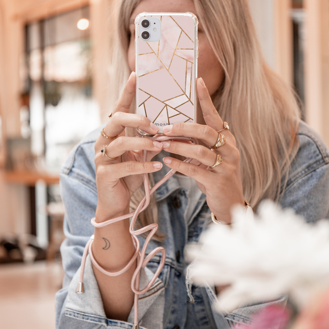 Une femme tient un téléphone avec une coque au design géométrique rose et un cordon rose.