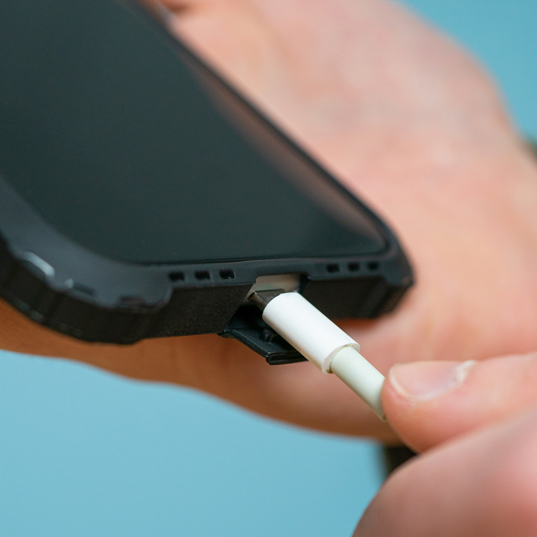 Close-up van een telefoon en oplader, met een kabel aangesloten op de telefoon.