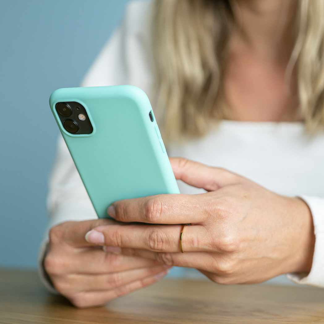 Vrouw houdt een turquoise telefoon vast in een zwarte hoes, met een gouden ring. Blauwe achtergrond.