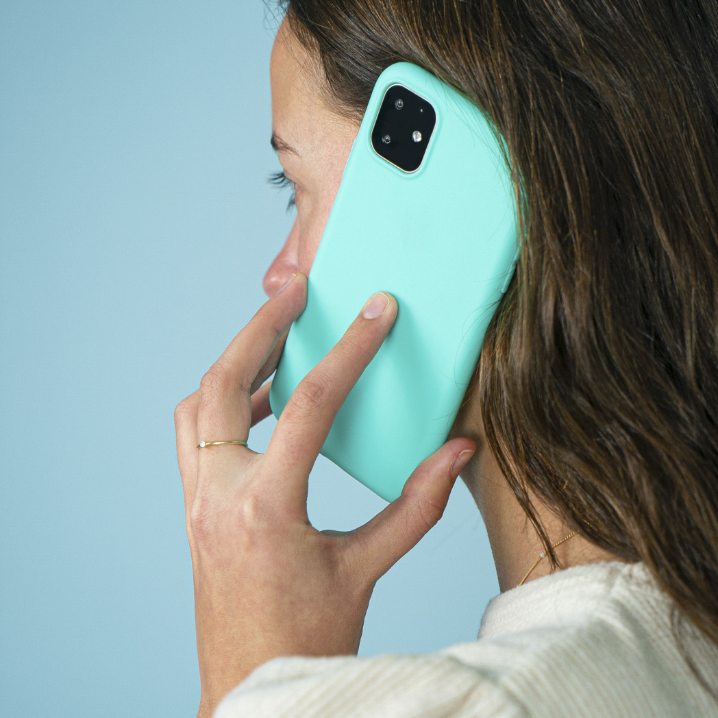 Een vrouw houdt een telefoon aan haar oor en praat. De telefoon is lichtgroen van kleur.