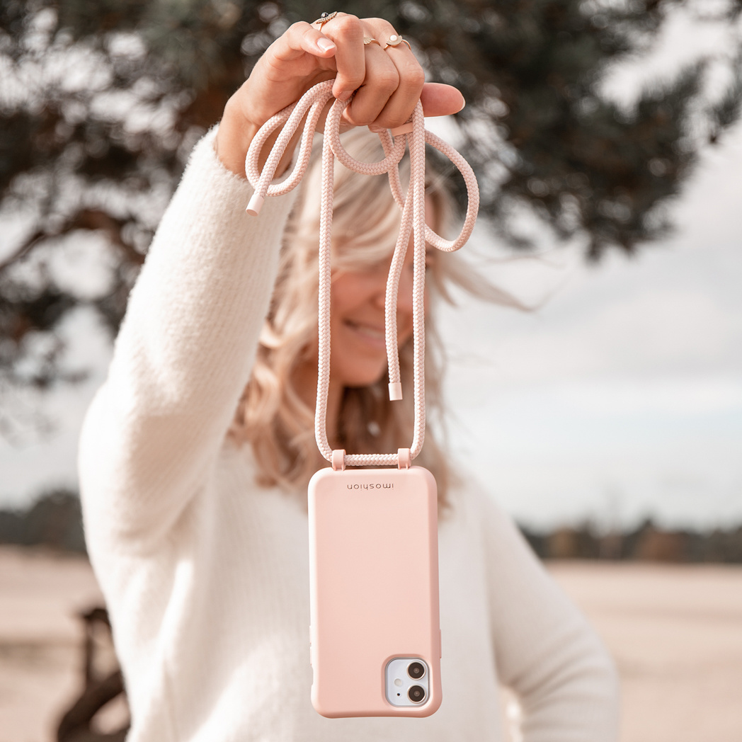 Vrouw houdt een roze telefoonhoesje met een koord vast, met een wazige achtergrond.