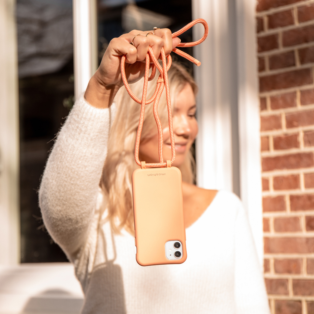 Vrouw die een telefoon vasthoudt met een oranje telefoonhoesje en bandje.