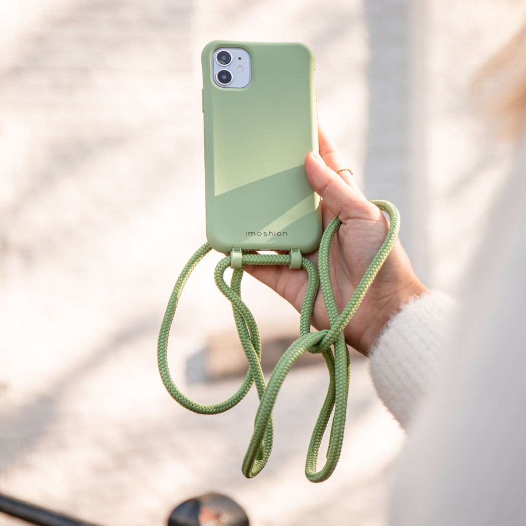 Main tenant une coque de téléphone vert clair avec une sangle verte assortie, sur un fond flou.