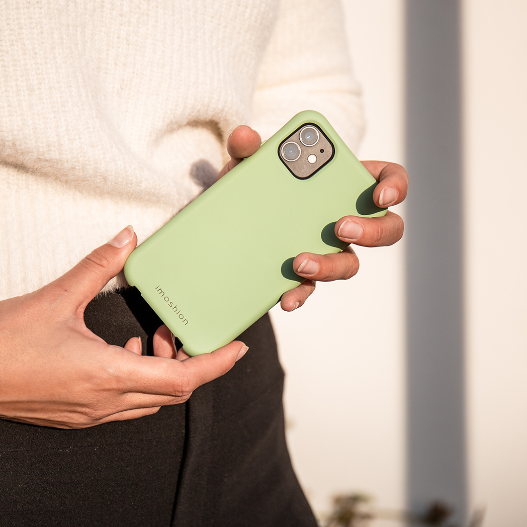 Une personne tient une coque de téléphone verte, montrant l'appareil photo du téléphone et la marque de la coque.
