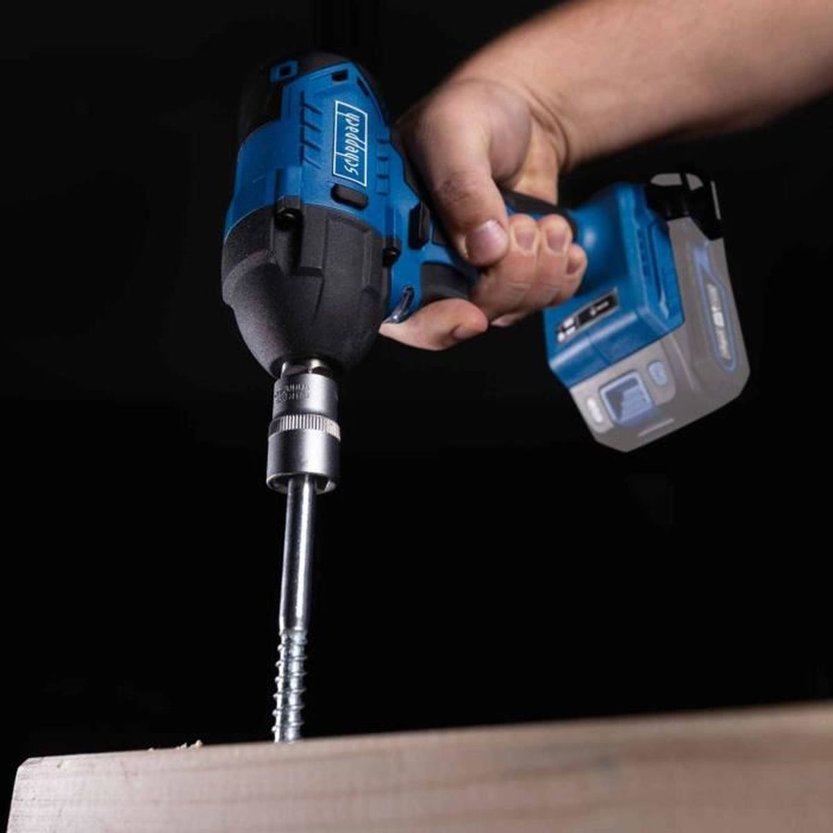 Een hand die een blauw-zwarte boormachine vasthoudt en een schroef in hout draait.