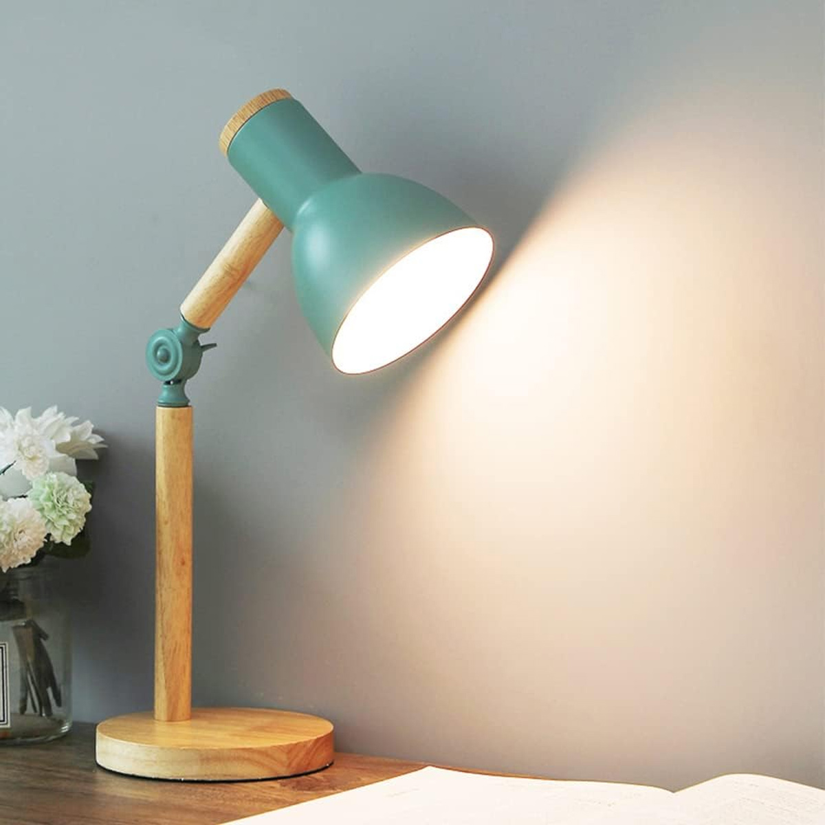 Schreibtischlampe. Sie hat einen grünen Lampenschirm, einen Holzarm und einen Sockel. Sie steht auf einem Schreibtisch.