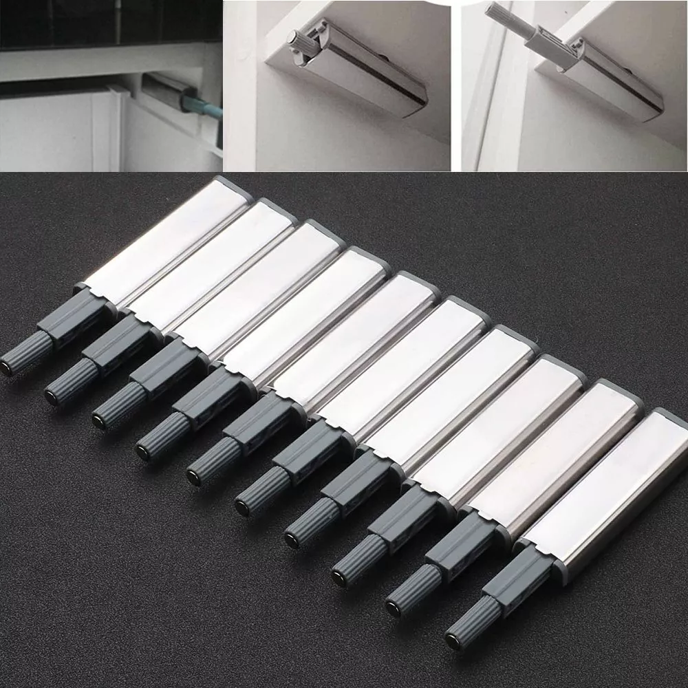 Mehrere Schranktür-Drucköffner, silber und grau, auf dunkler Oberfläche.