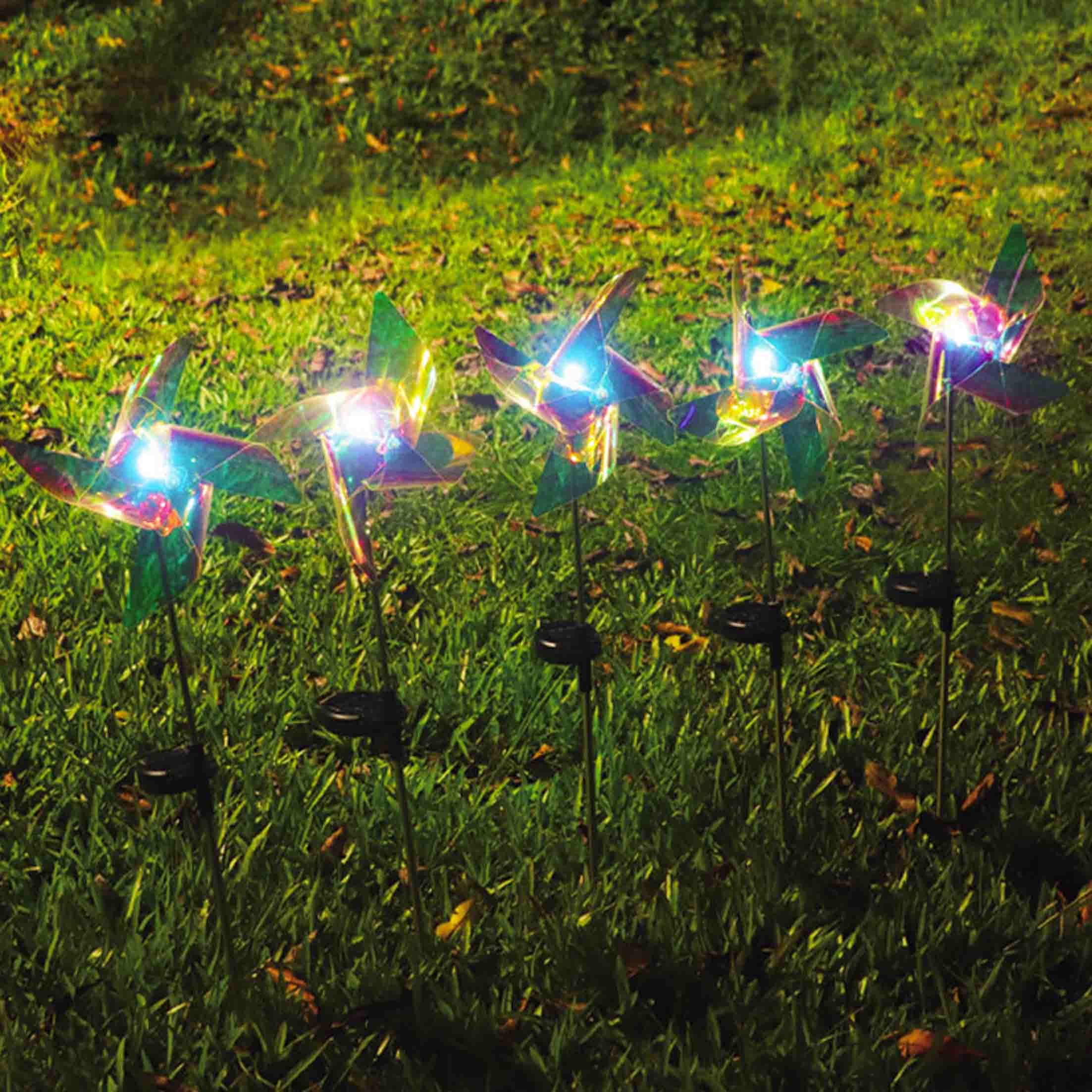 Vier beleuchtete Gartenstecker mit Windrädern im Gras.