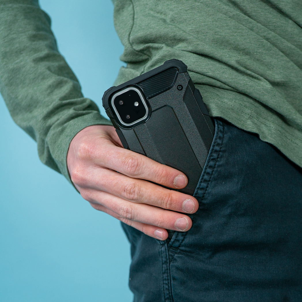 Een hand die een zwarte telefoon met een hoesje in een zak steekt. De achtergrond is blauw.