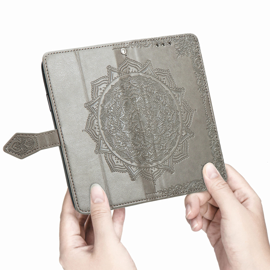 Handen die een grijze telefoonhoes vasthouden met een reliëf mandala-ontwerp op de voorkant.