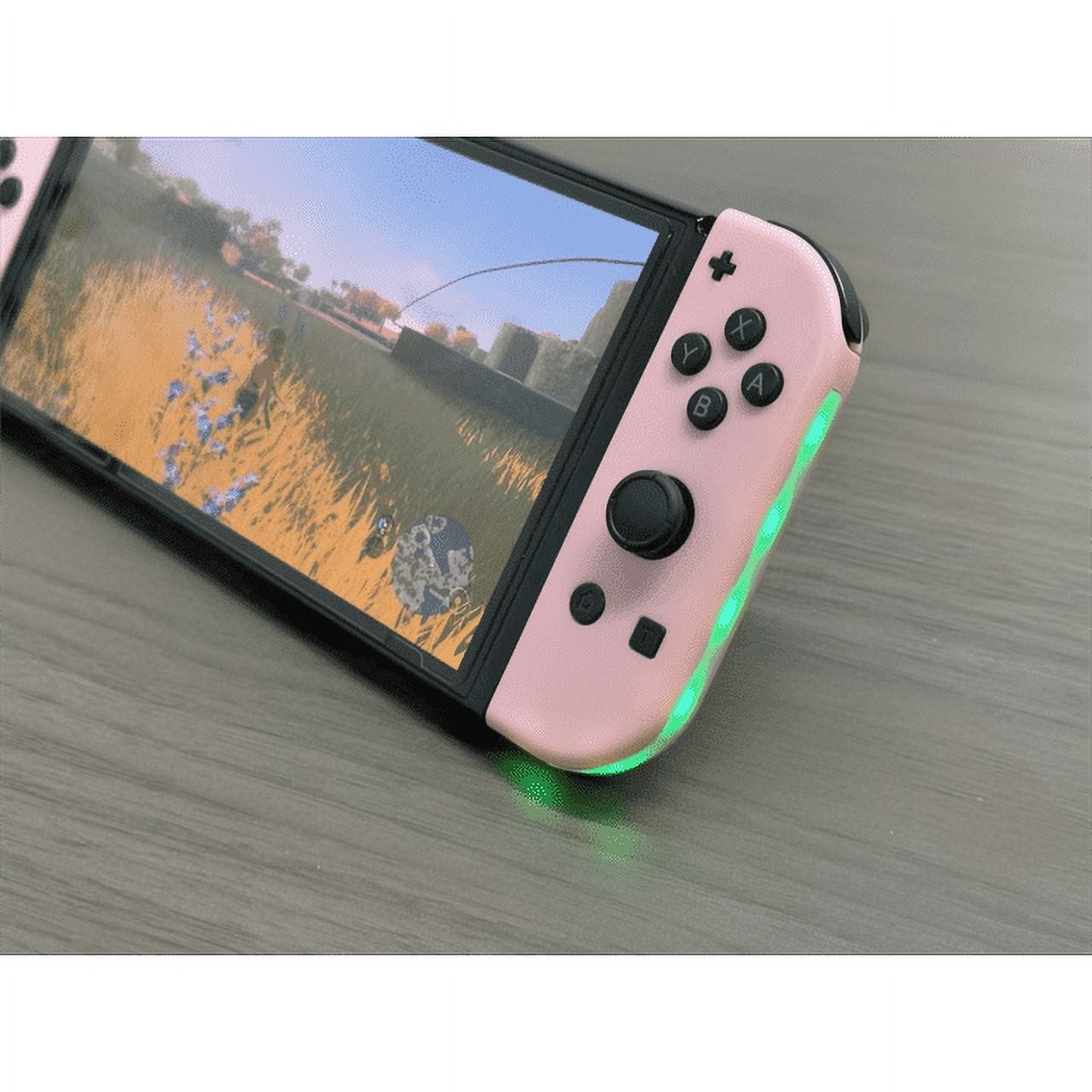 Pink Nintendo Switch mit Spielbildschirm. Joy-Cons pink mit grünen Lichtern. Grauer Tisch.