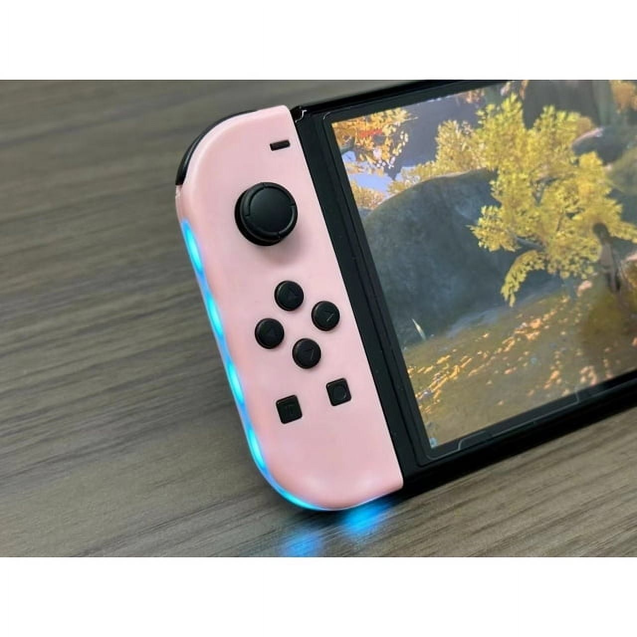 Rosa Nintendo Switch-Controller mit Bildschirm, der eine Waldszene zeigt; auf Holzoberfläche.