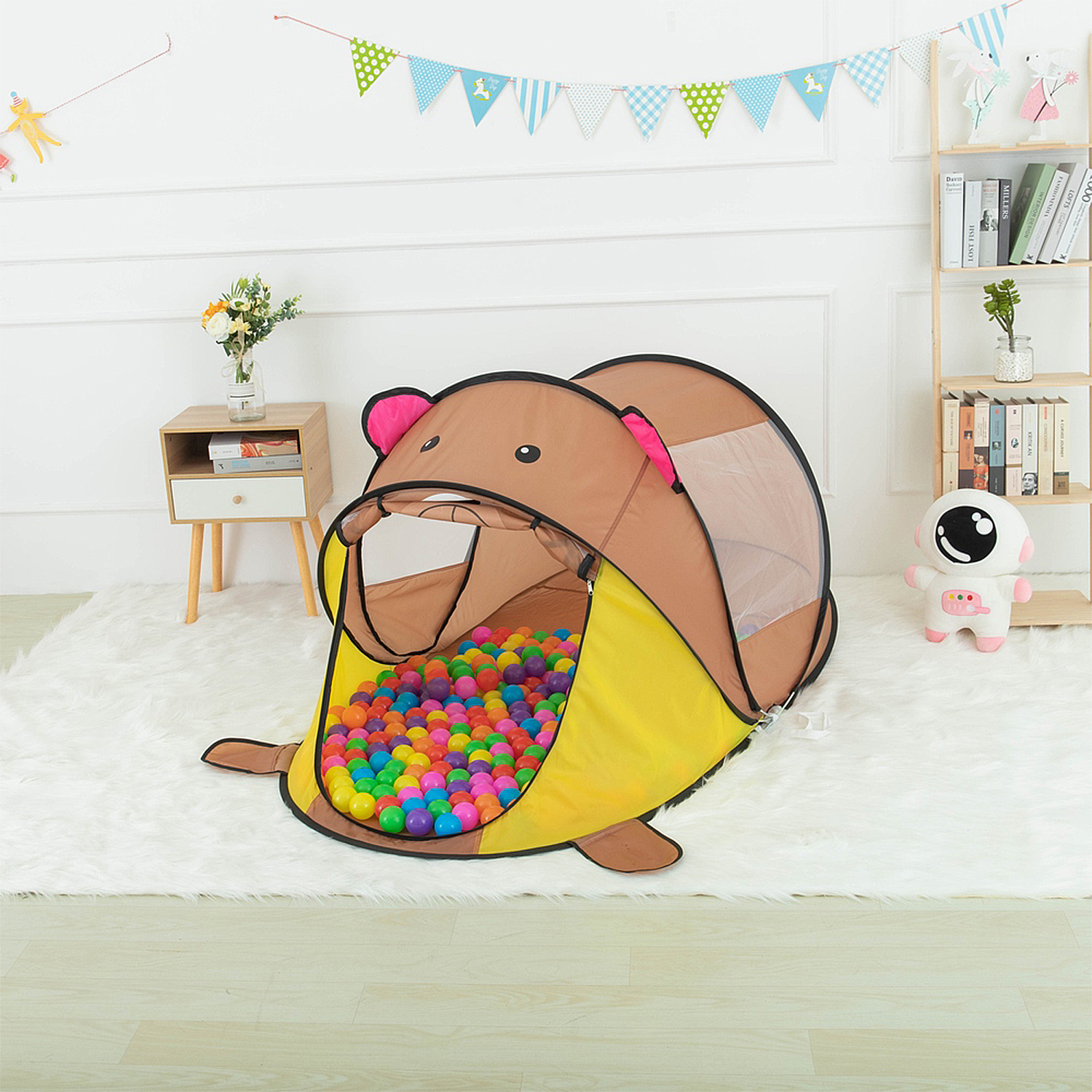 Tienda de juegos con forma de oso marrón llena de bolas de colores, sobre alfombra blanca.