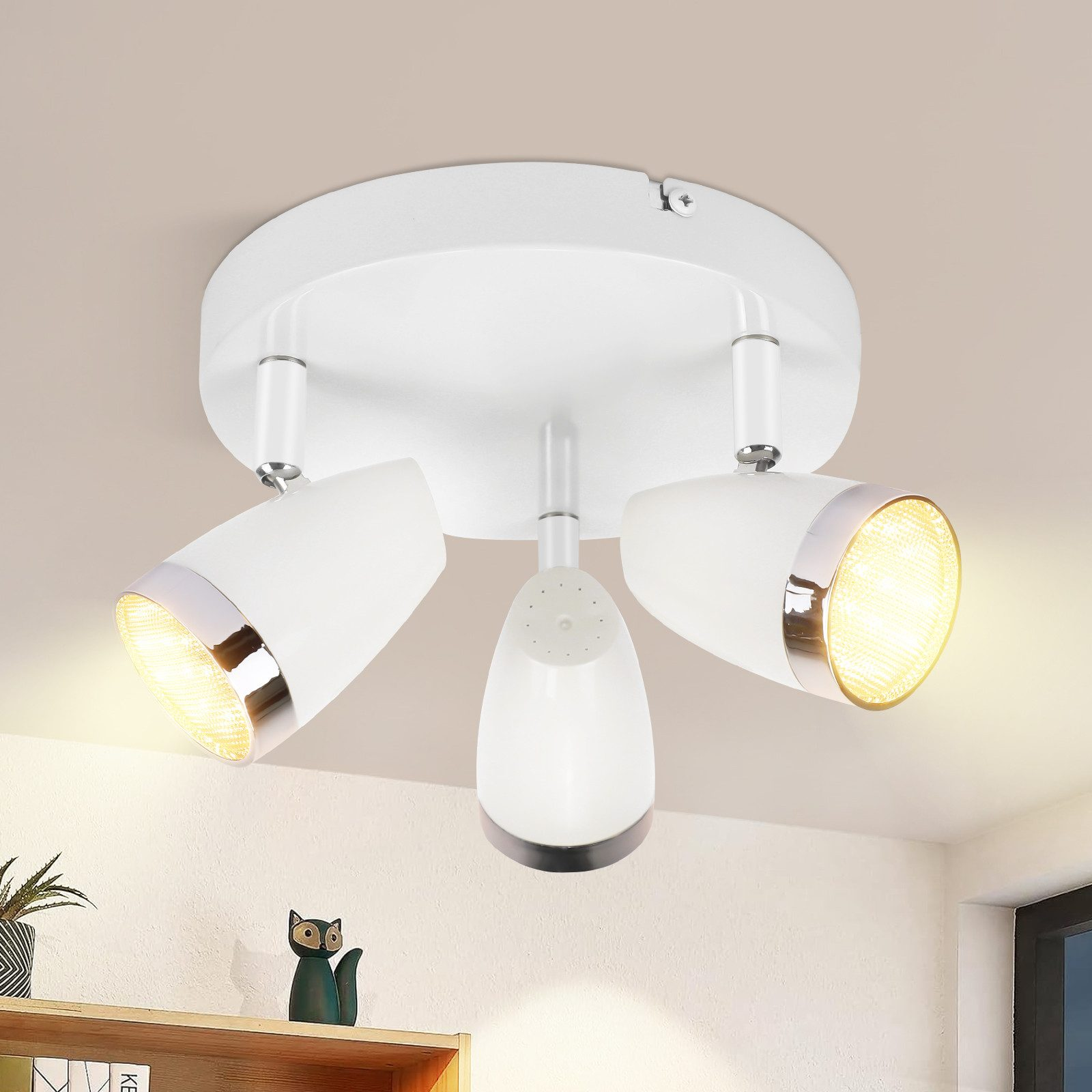 Lampada da soffitto bianca con tre faretti orientabili. Le luci sono accese e puntano verso il basso.