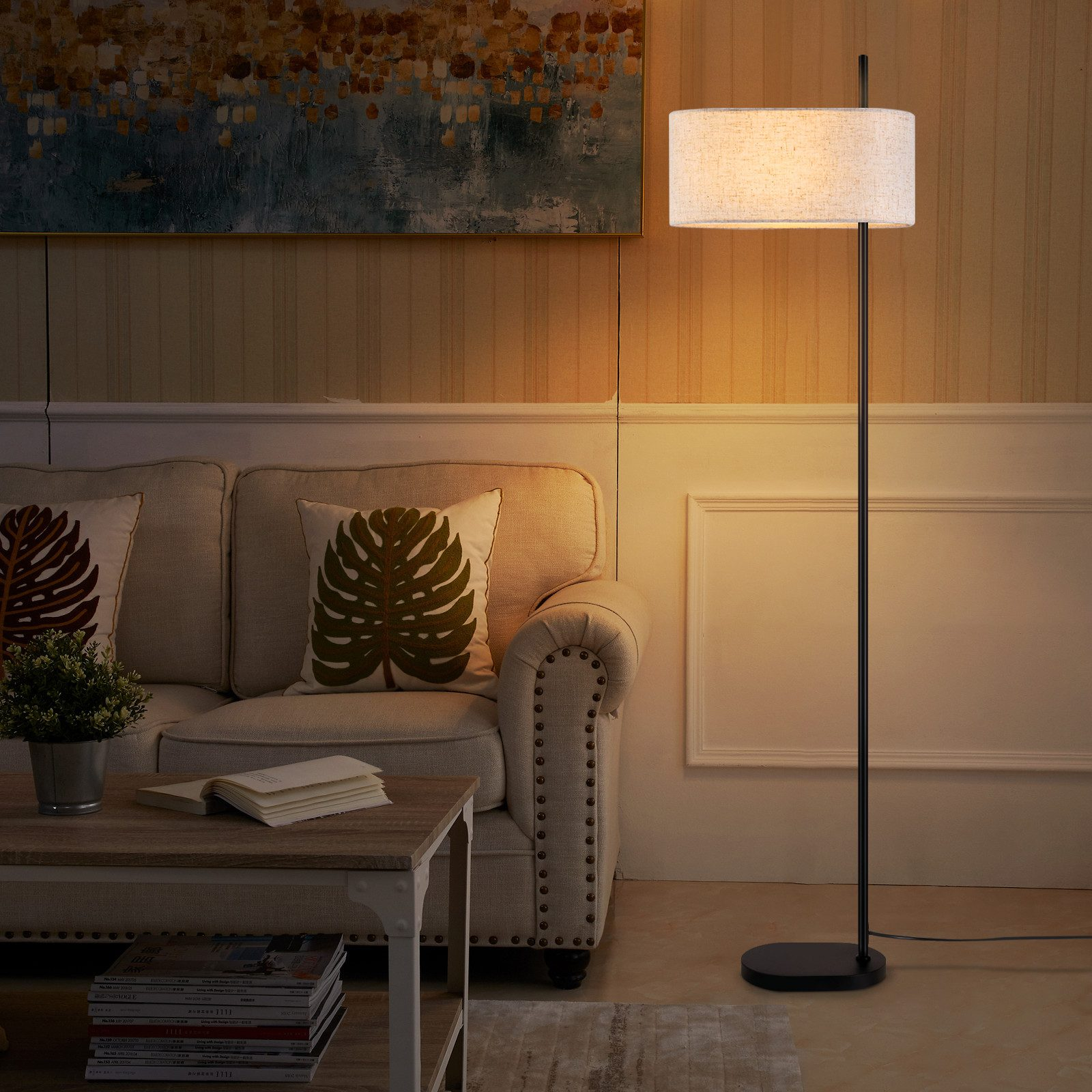 Una lampada da terra accanto a un divano e un tavolo. La lampada ha un paralume beige.