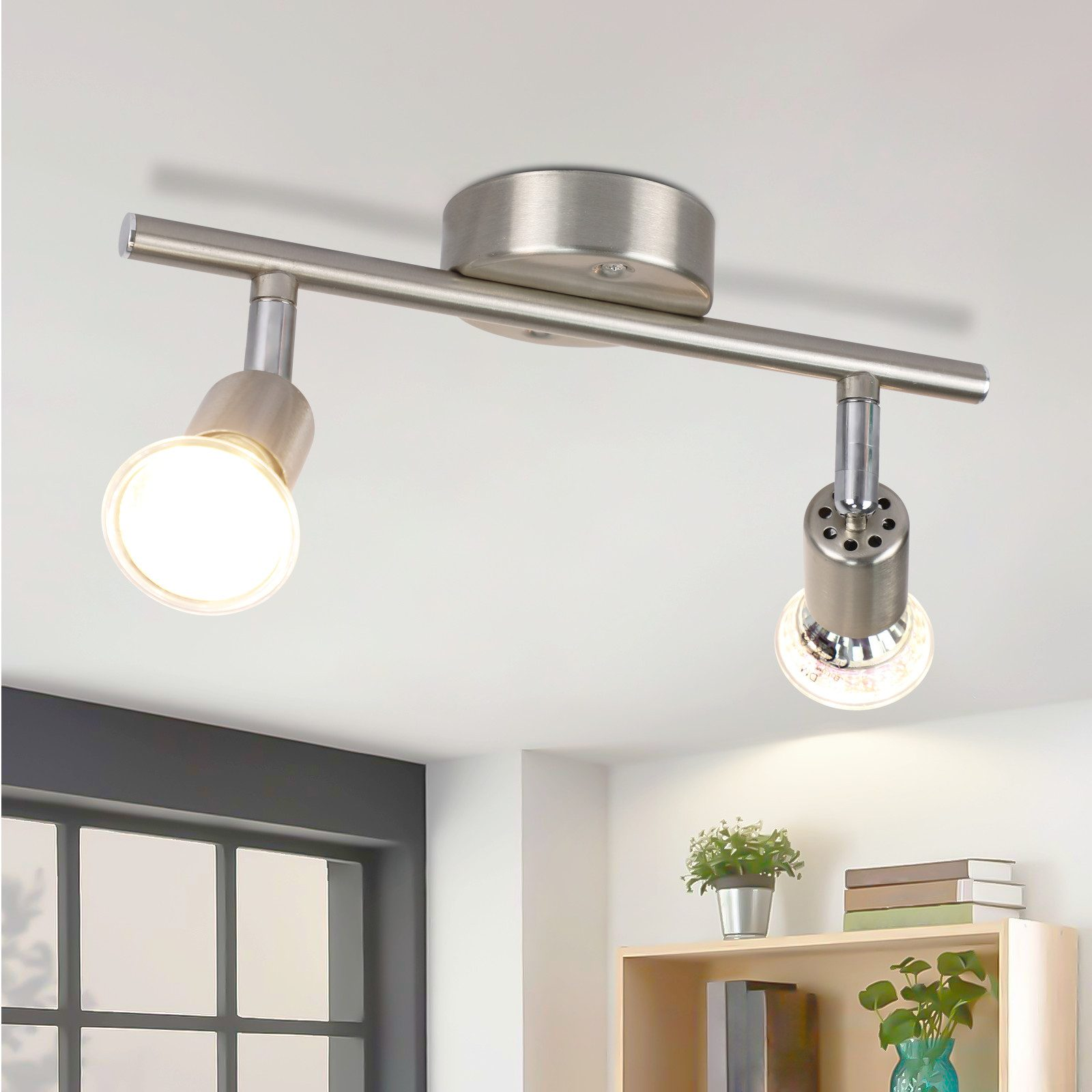 Un apparecchio a faretti da soffitto a due luci in una stanza con una pianta e opere d'arte.