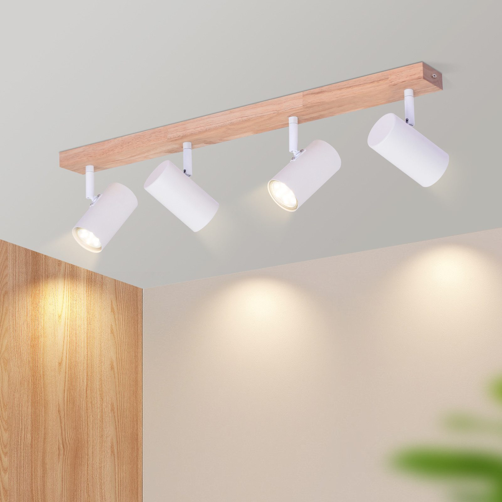 Quattro faretti bianchi a soffitto su una trave di legno. Le luci sono accese, che illuminano verso il basso.