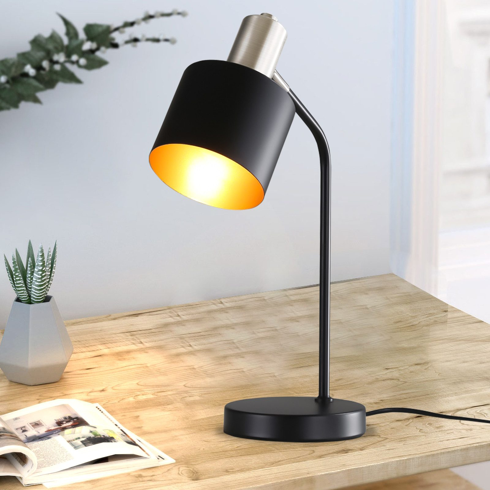 Czarno-srebrna lampa biurkowa ze złotym wnętrzem, rośliną i książką.