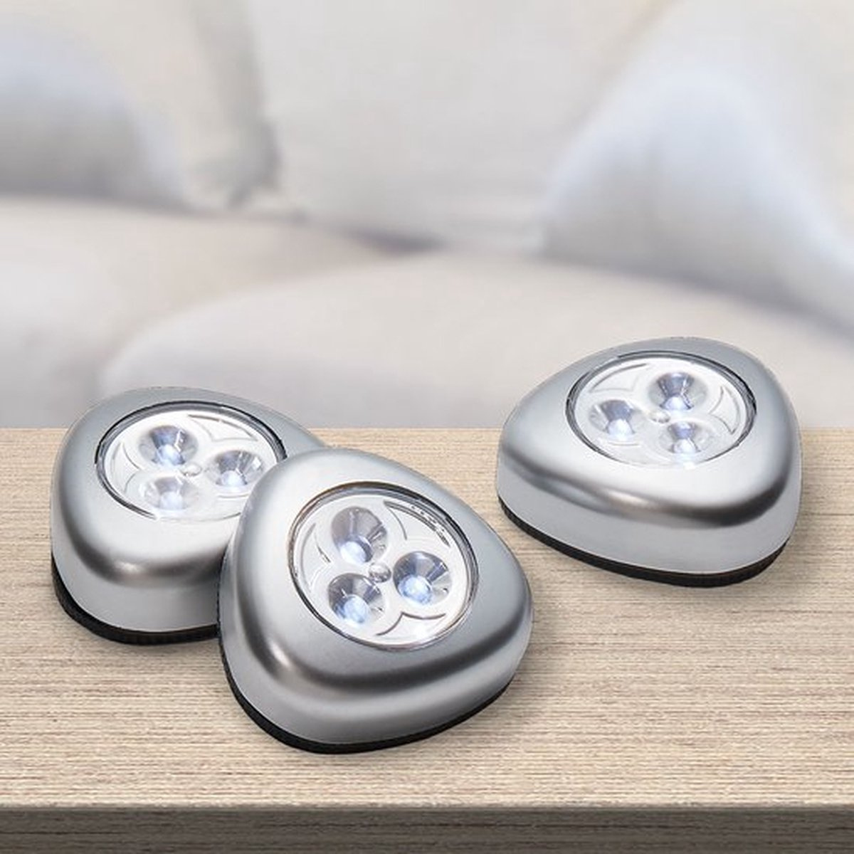 Drei silberne LED-Leuchten auf Holz. Hintergrund ist verschwommenes Weiß.