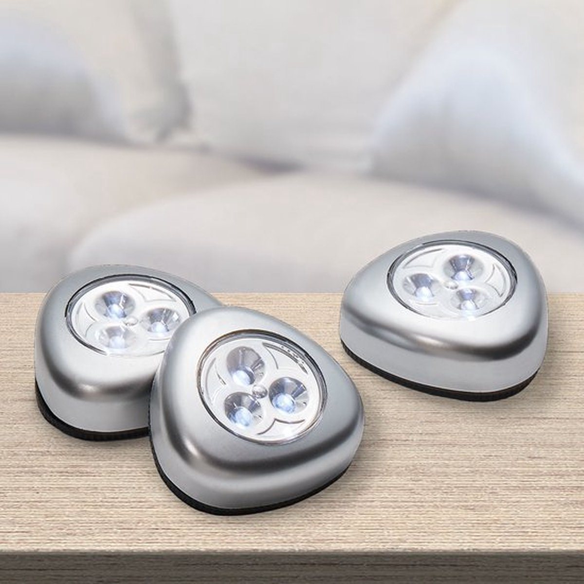 Drei silberne LED-Leuchten auf einem Holztisch mit verschwommenem Hintergrund.