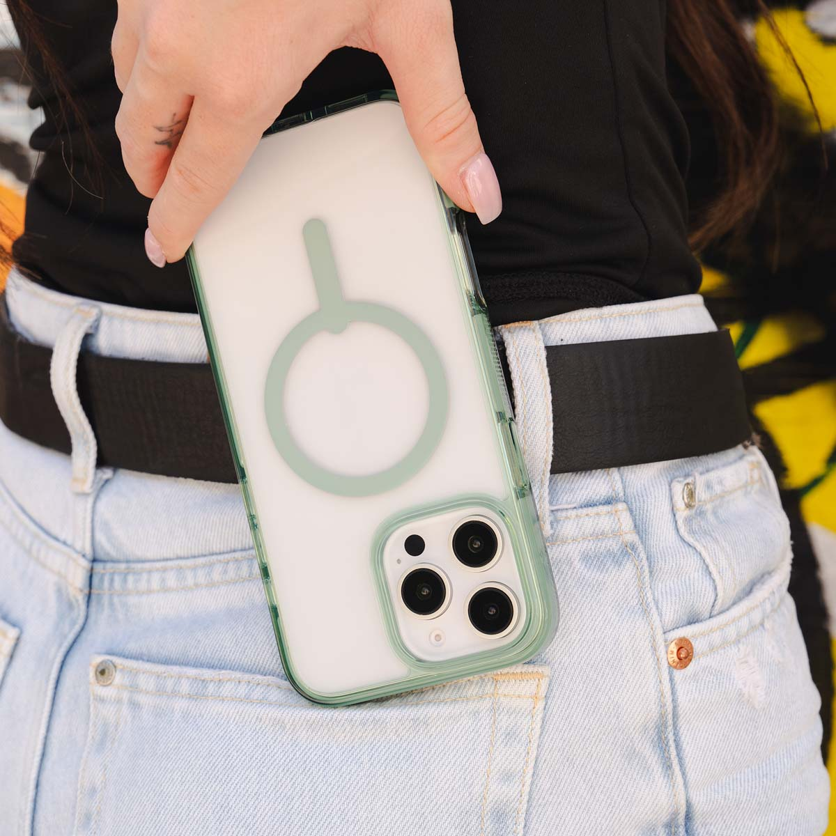 Een hand houdt een telefoon in een hoesje. De hoes is transparant met een groene ring en de telefoon zit in een zak.