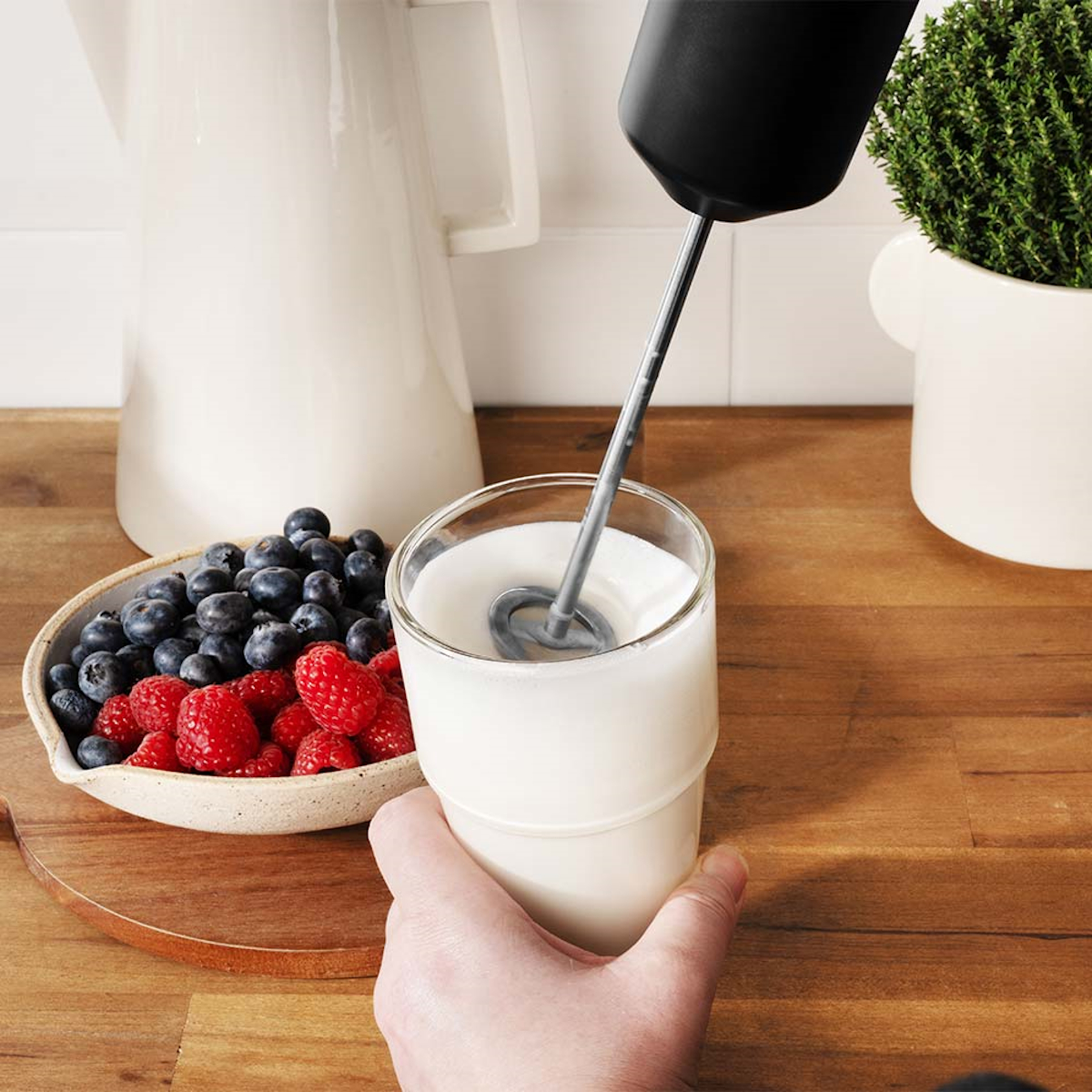 Hand, die ein Glas mit Milch hält, die mit einem Milchaufschäumer verrührt wird.