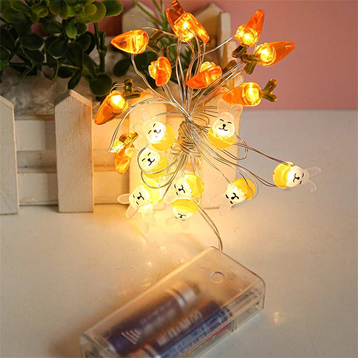 Lichterkette mit Hasen- und Karotten-Dekorationen. Lichter sind gelb. Ein Akku-Pack ist unten.