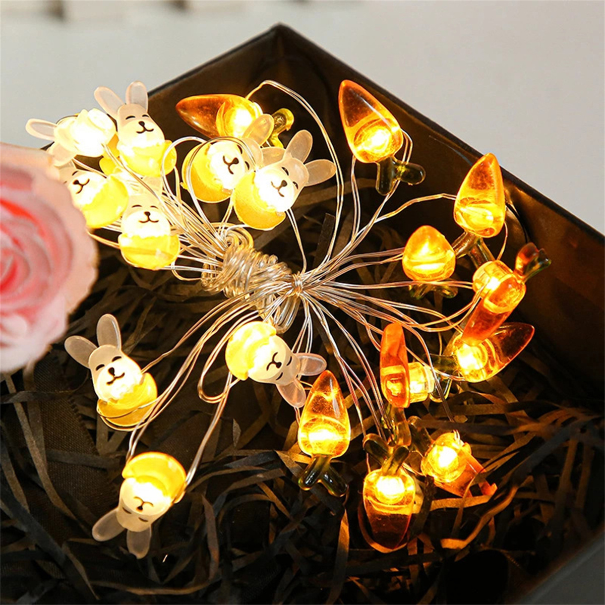 Lichterkette mit Hasen- und Karotten-Dekorationen, angeordnet in einer dunklen, geschenkboxartigen Umgebung.