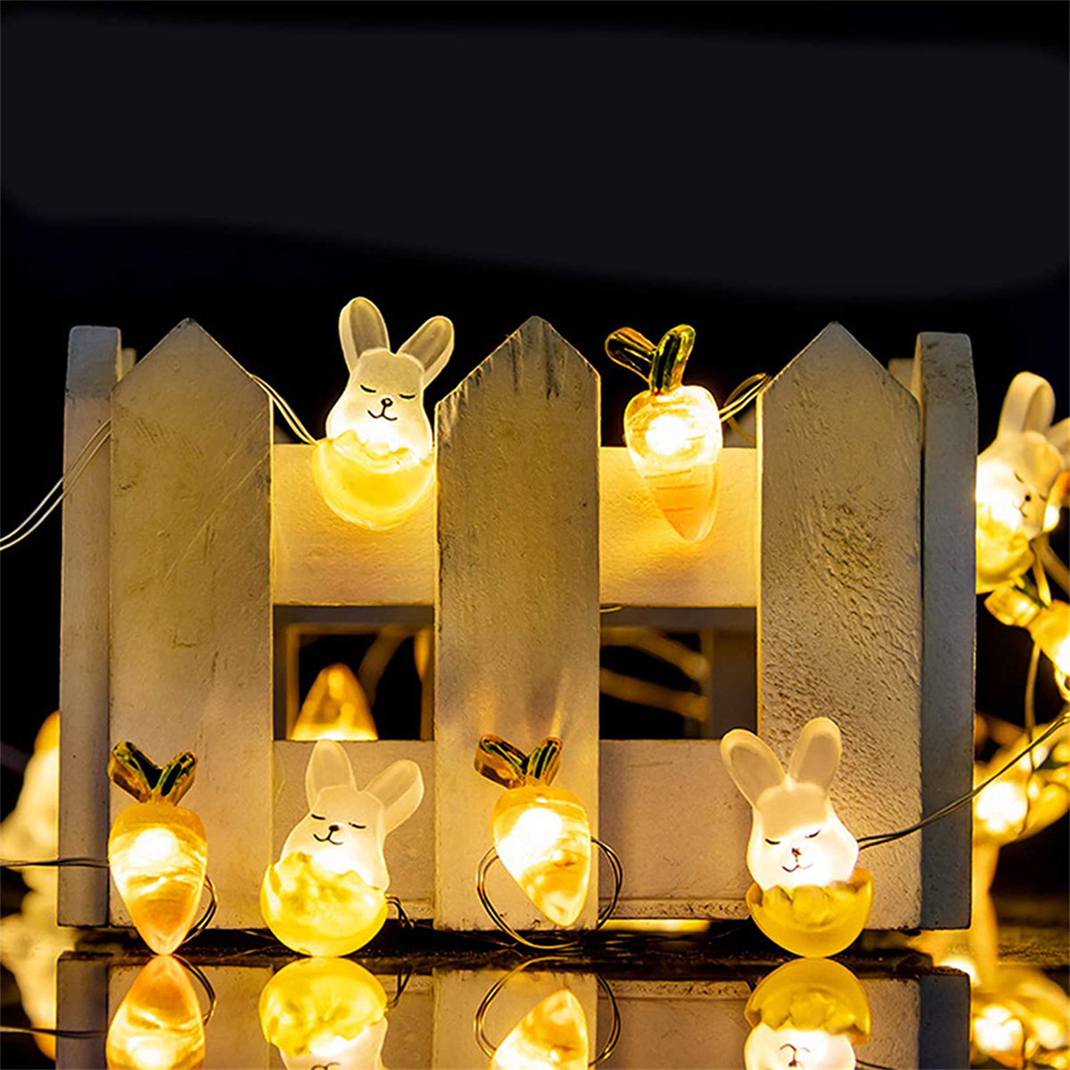 Dekorative Lichterketten mit Hasen- und Karottendesigns, angeordnet entlang eines weißen Zauns.
