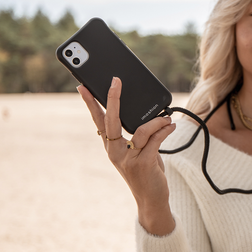 Vrouw die een zwarte telefoon met een riem vasthoudt, met een strandachtergrond.