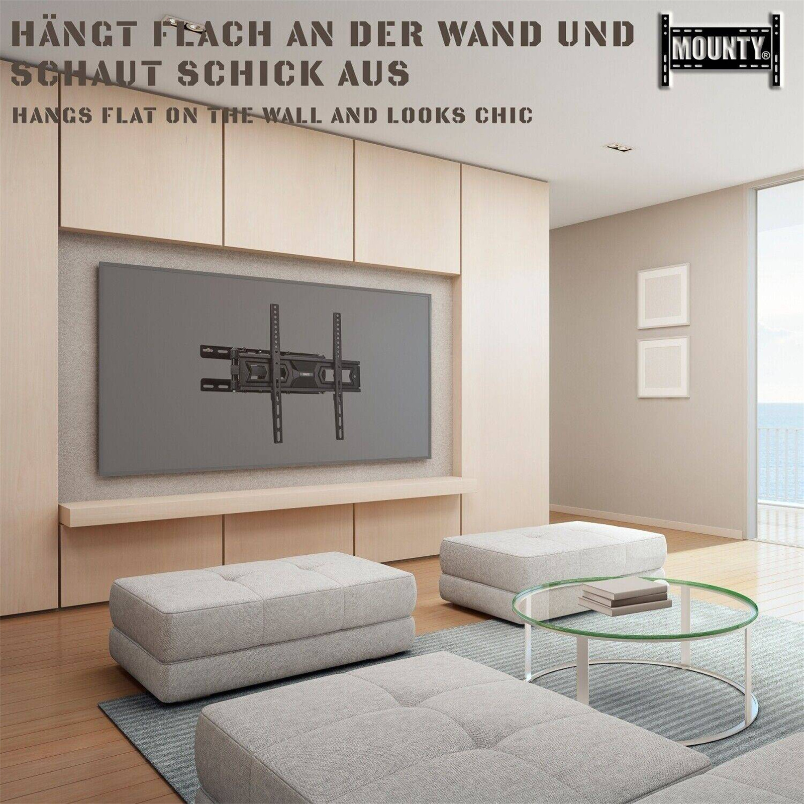 Ein Wohnzimmer mit einem an der Wand montierten Fernseher, drei grauen Ottomanen und einem Glastisch mit einer Pflanze darauf.