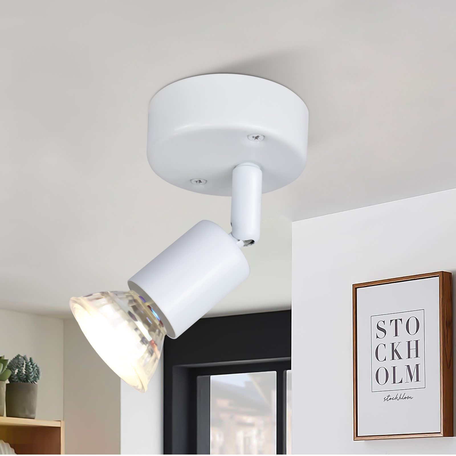 Un faretto bianco montato a soffitto. Una cornice è visibile sulla parete.