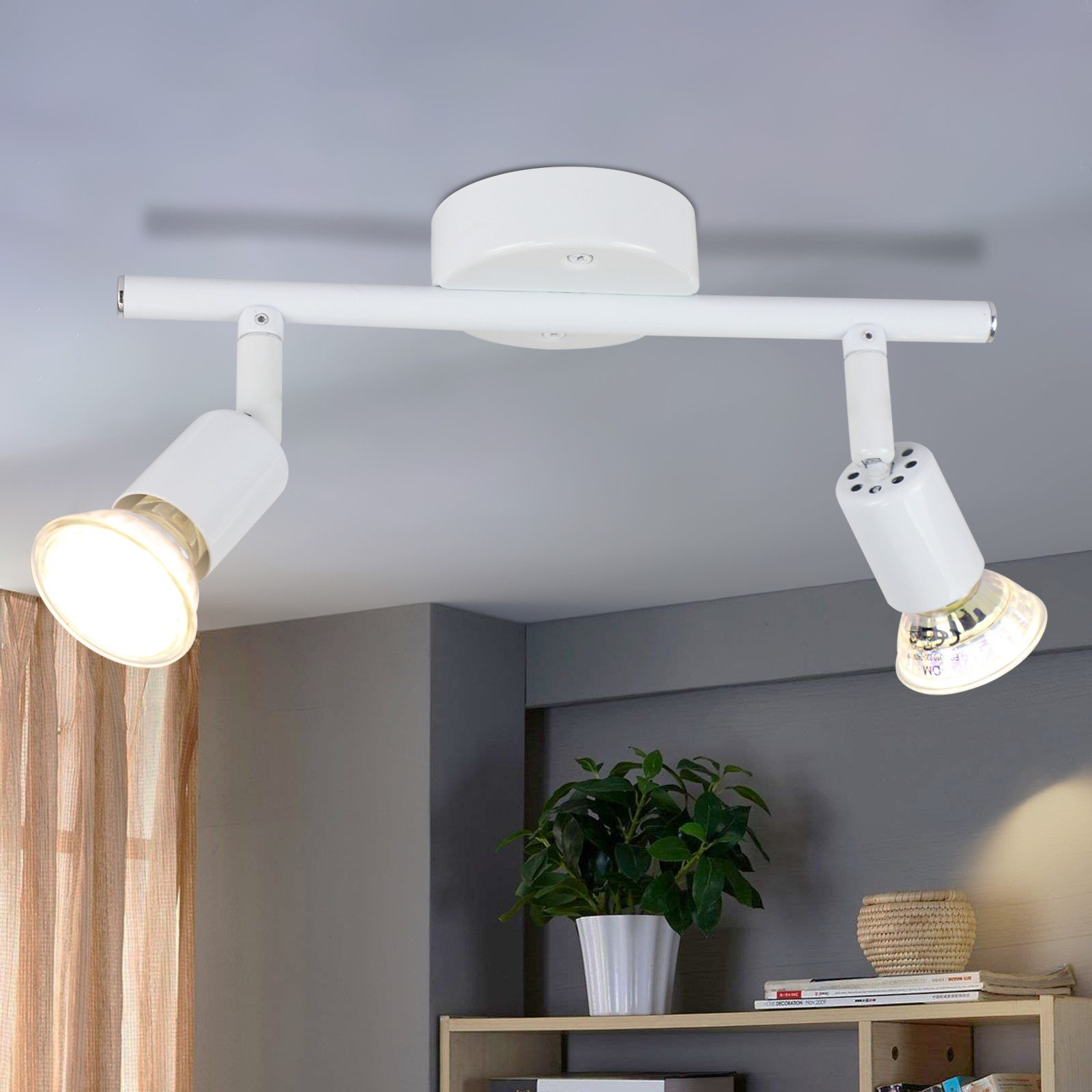Faretti bianchi a soffitto su una barra bianca. Pianta e libro sullo scaffale. Sfondo muro grigio.