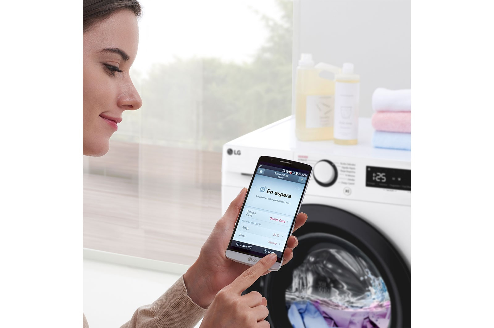 Kobieta używa telefonu, pralka w tle. Widoczne butelki i ręczniki.