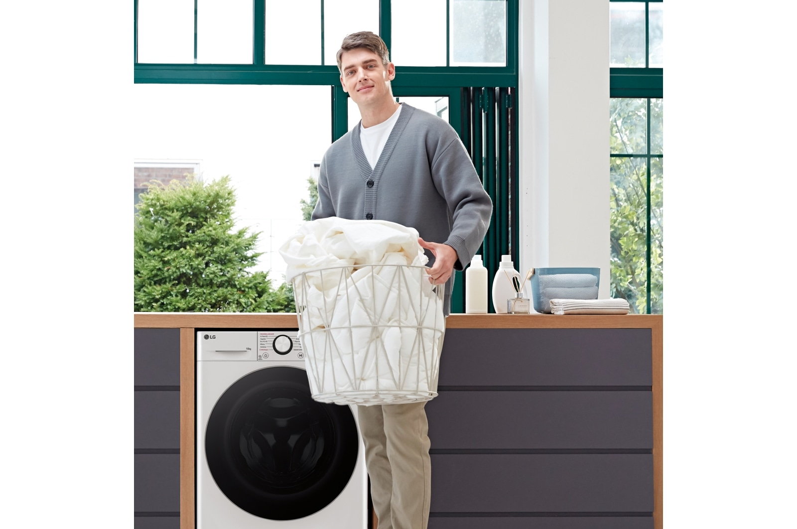 Mężczyzna trzymający kosz białych ręczników, stojący obok pralki. Otoczenie pralni.