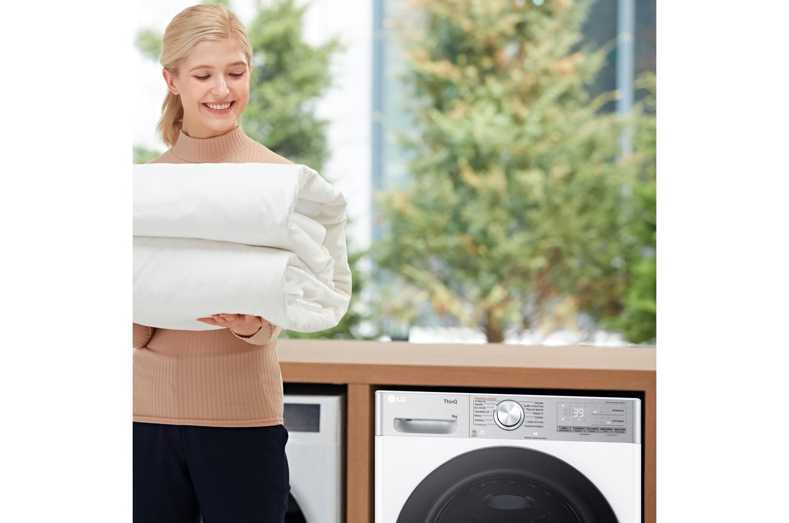Kobieta trzymająca złożone białe prześcieradła przed pralką.