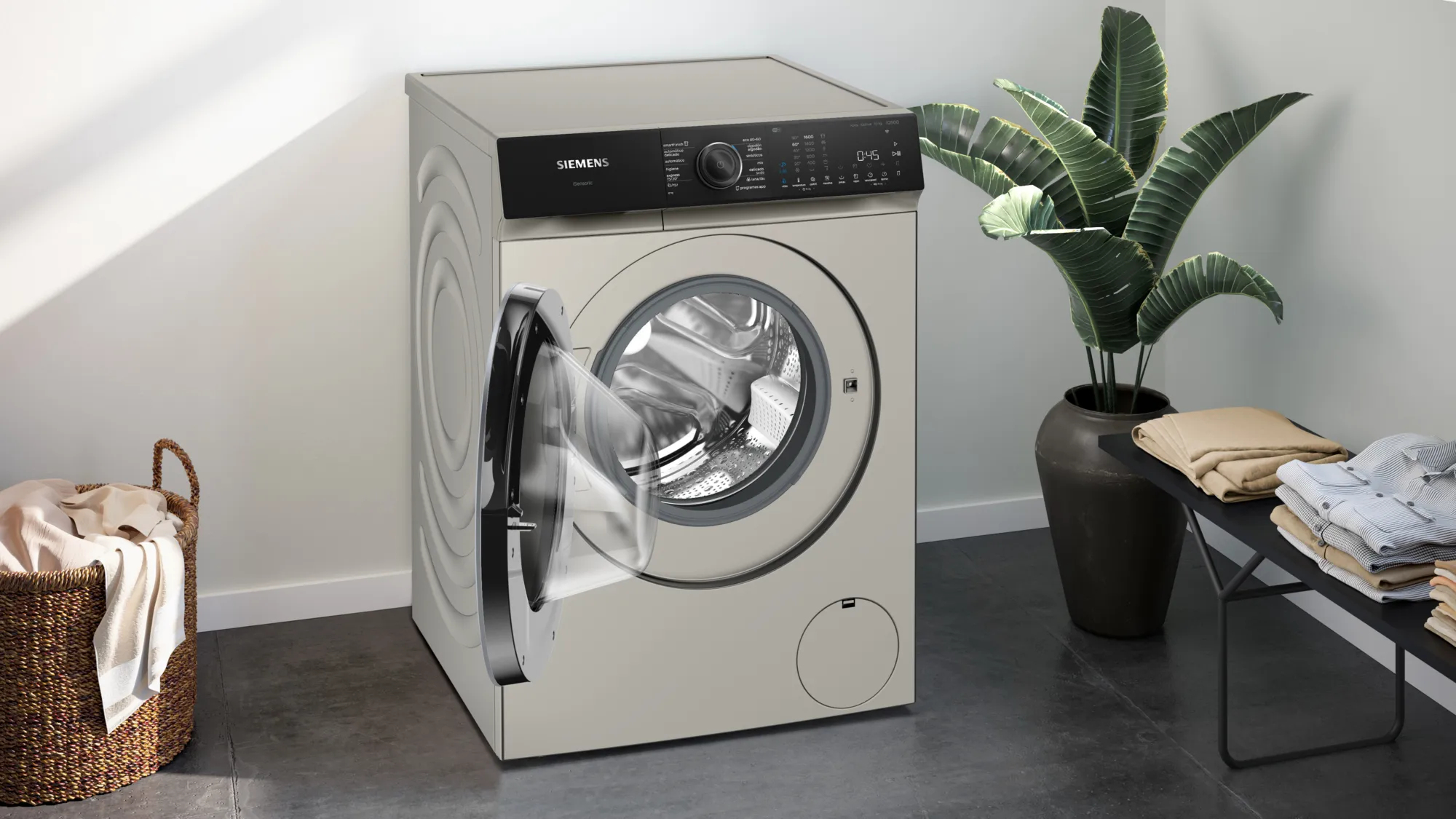 Lavadora Siemens beige, puerta abierta, con cesta de ropa y planta al lado.