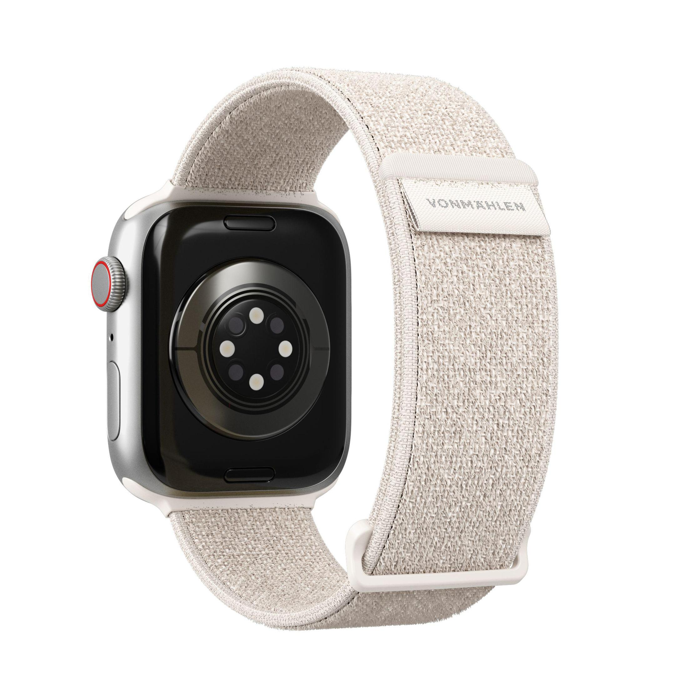 Srebrny Apple Watch z kremowym paskiem. Zegarek pokazuje tył, z czerwonym przyciskiem z boku.