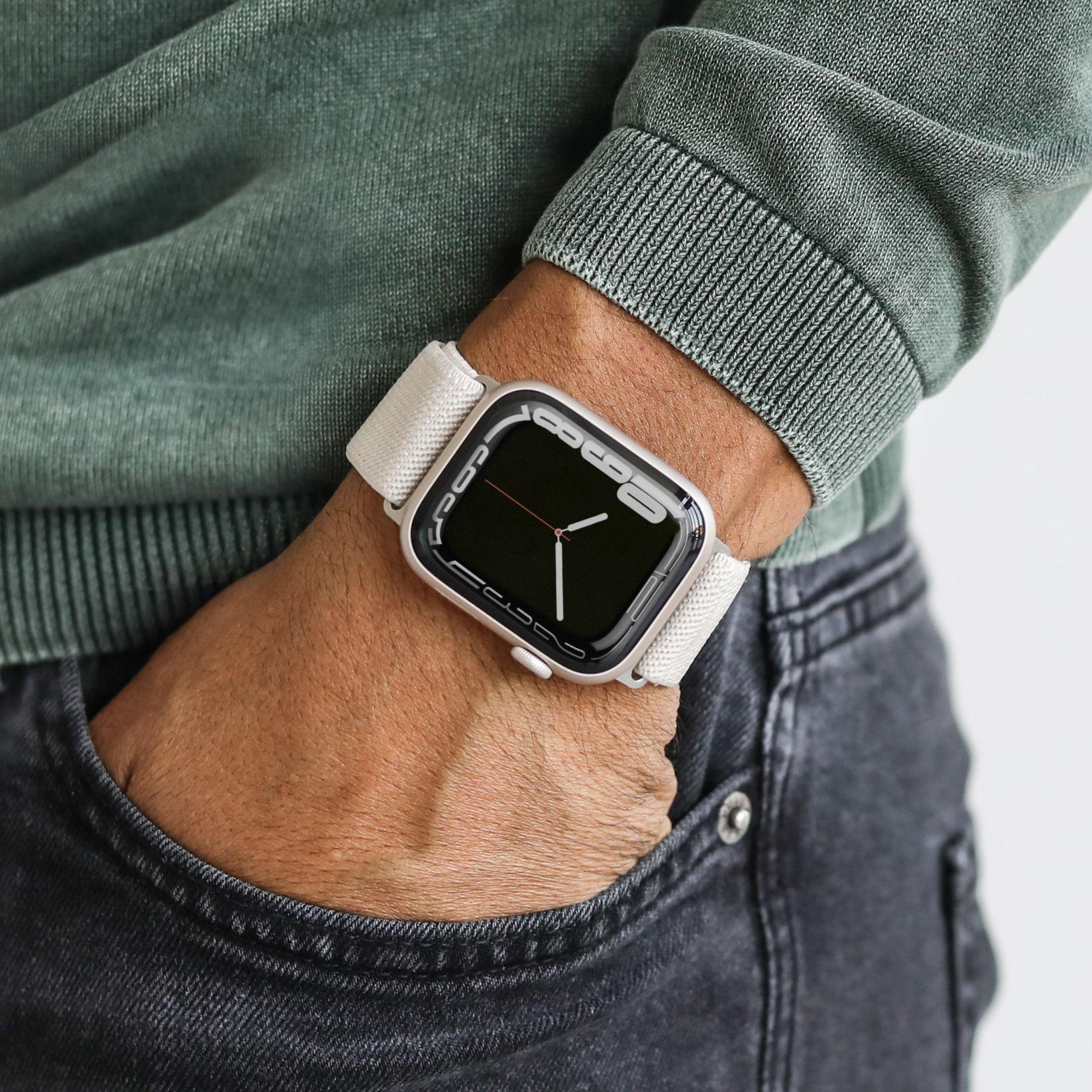 Osoba w zielonym swetrze i srebrnym Apple Watch z białym paskiem na nadgarstku.