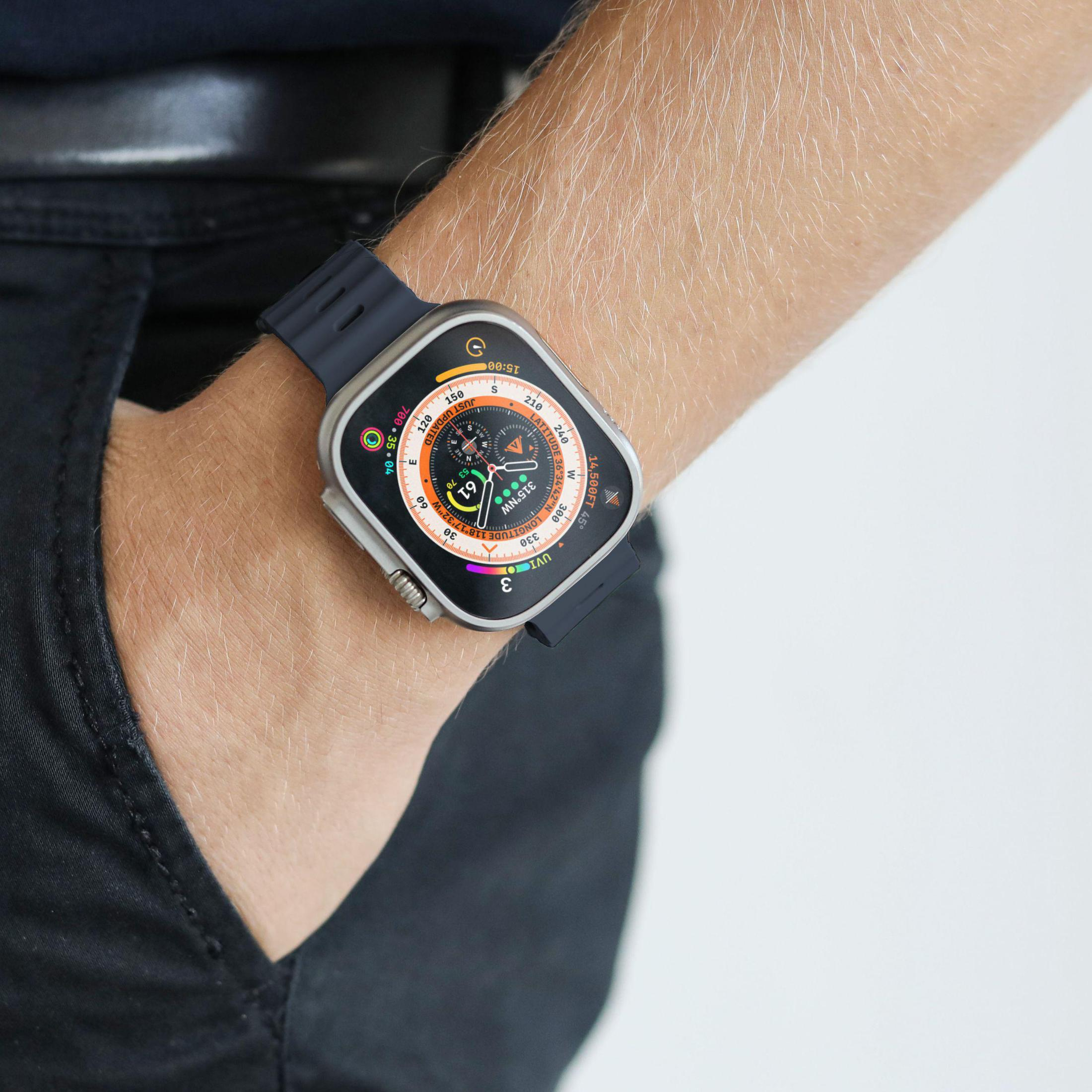 Nadgarstek osoby noszącej smartwatch z czarnym paskiem. Tarcza zegarka pokazuje różne punkty danych.