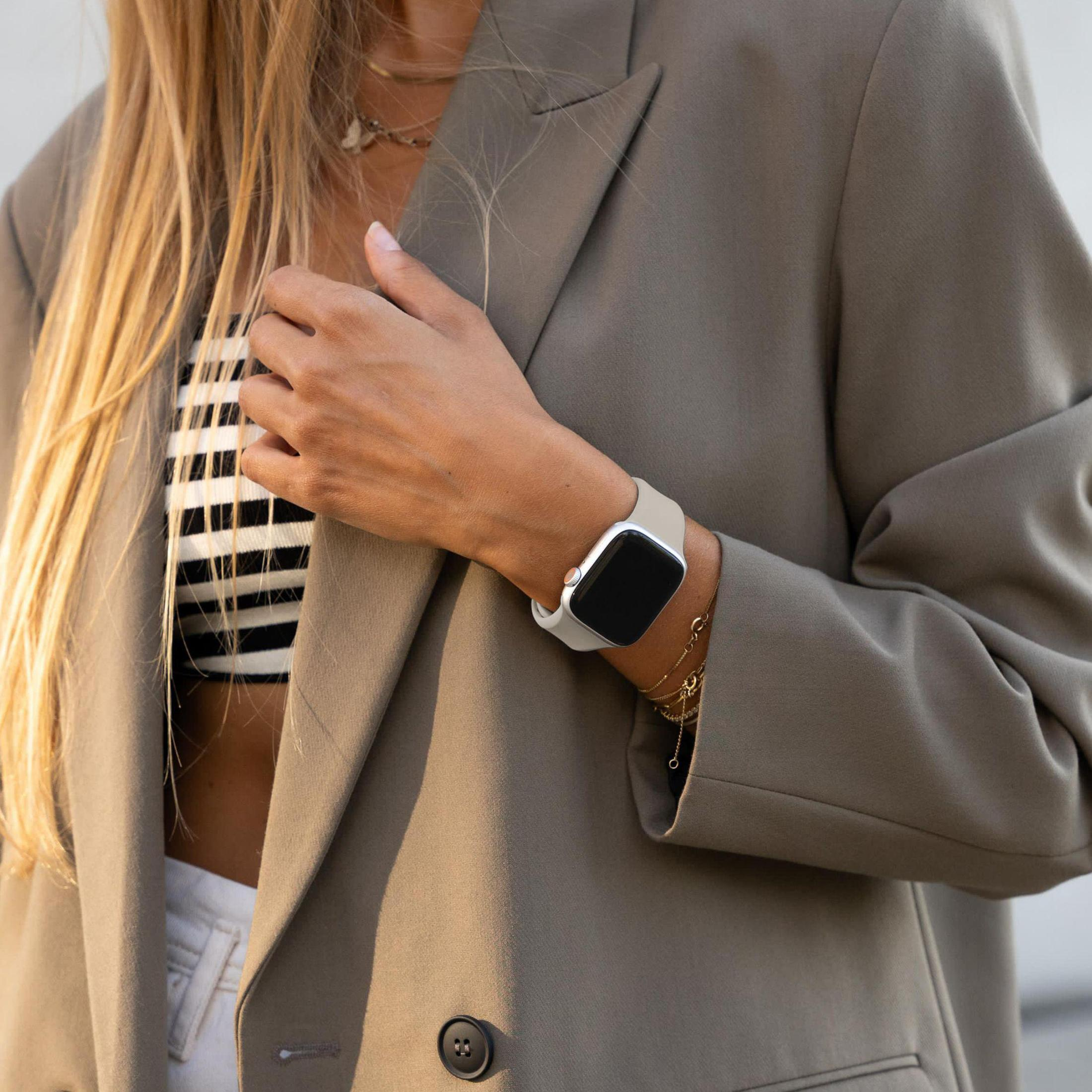 Una donna indossa un blazer e un orologio con cinturino bianco al polso. La sua mano è visibile.