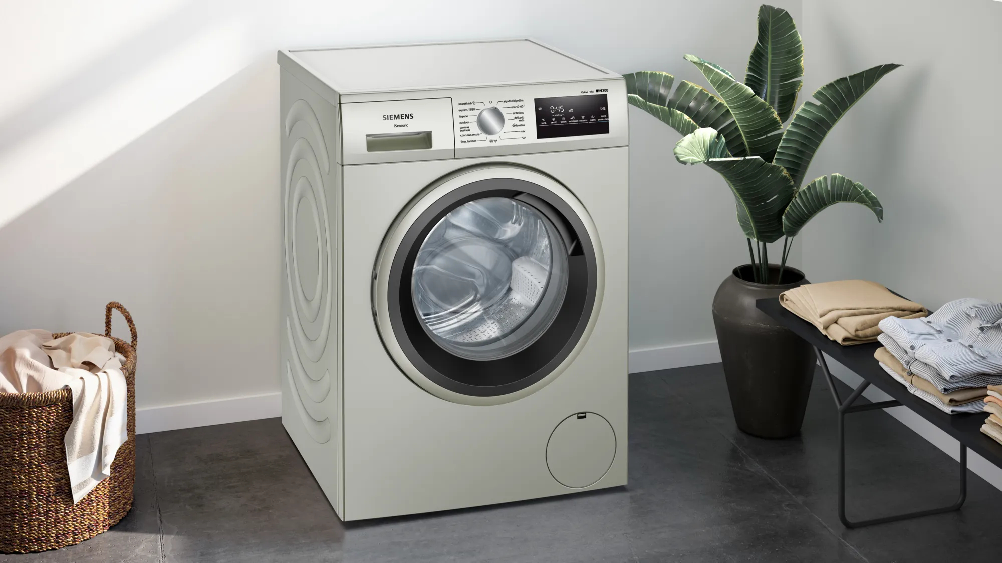 Srebrna pralka Siemens w pokoju. Są rośliny, kosz i ubrania.
