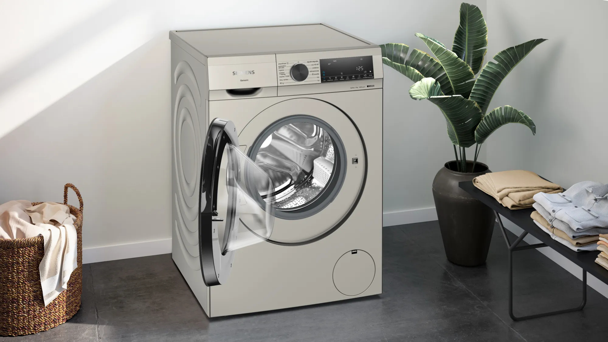 Lavadora con puerta abierta, cesta de ropa y plantas. Tonos beige y luz natural.