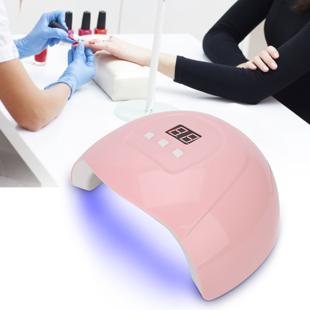 Eine rosa Nageltrocknungslampe auf einem weißen Tisch. Eine Person lackiert Nägel. Hintergrund: eine weiße Oberfläche.