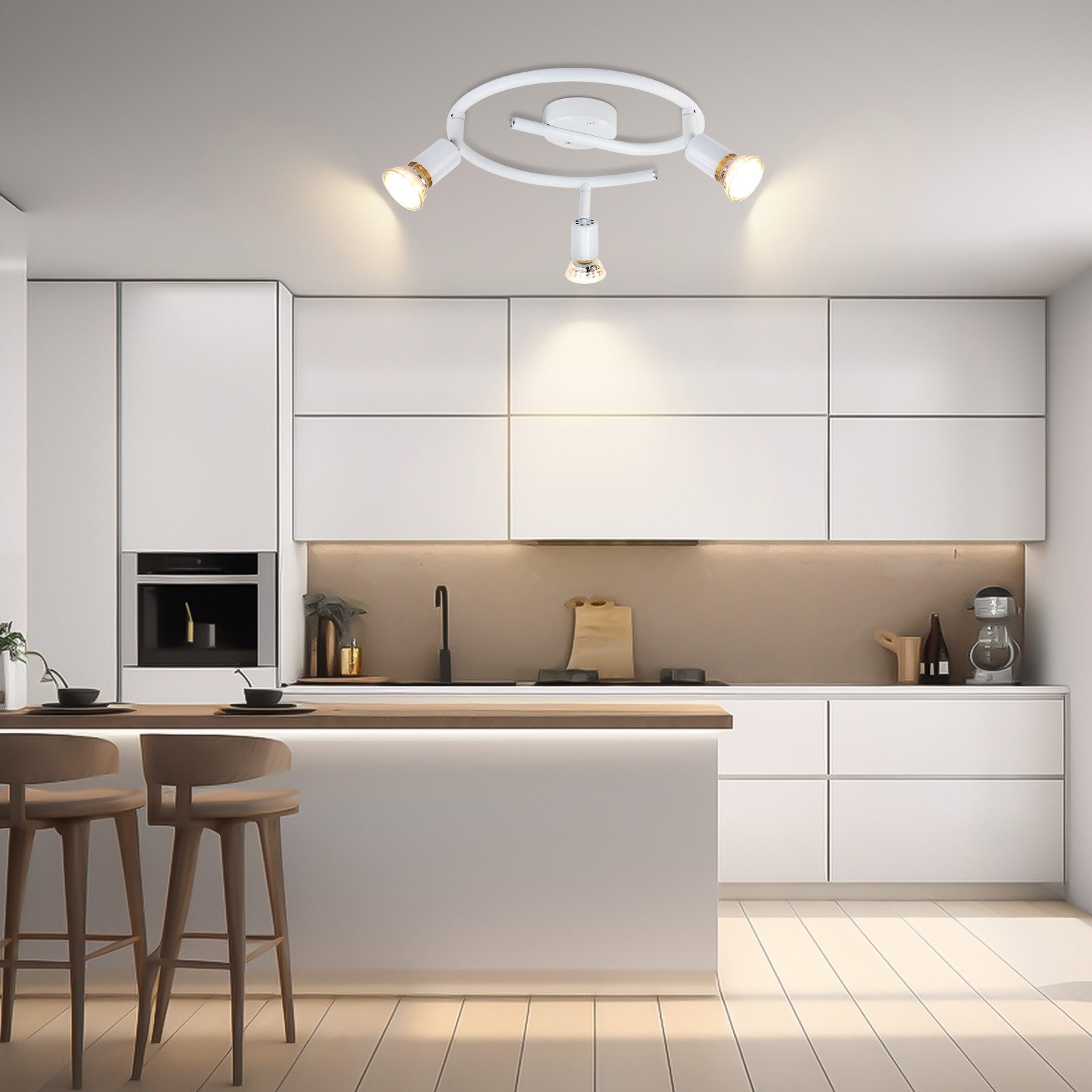 Cucina bianca con tre faretti. Un piano di lavoro in legno, con due sgabelli. Armadi e cassetti bianchi.