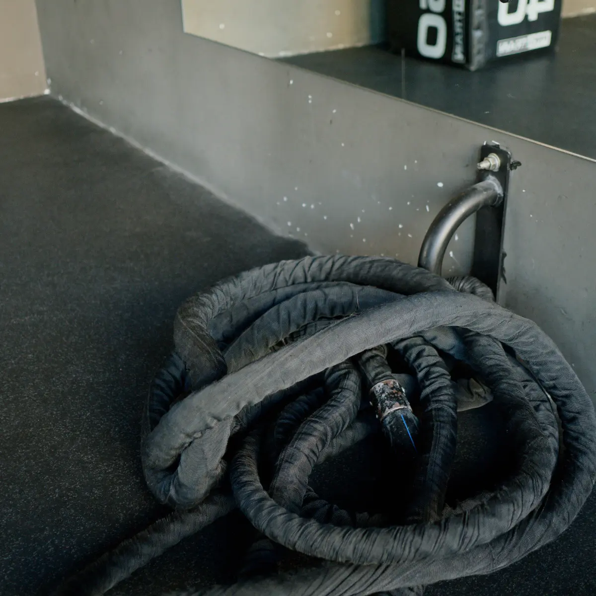 Corde noire enroulée sur un sol noir. Un miroir et une barre murale sont en arrière-plan.