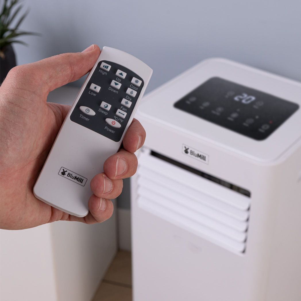 A person holding a white remote control pointing towards a white air conditioner.