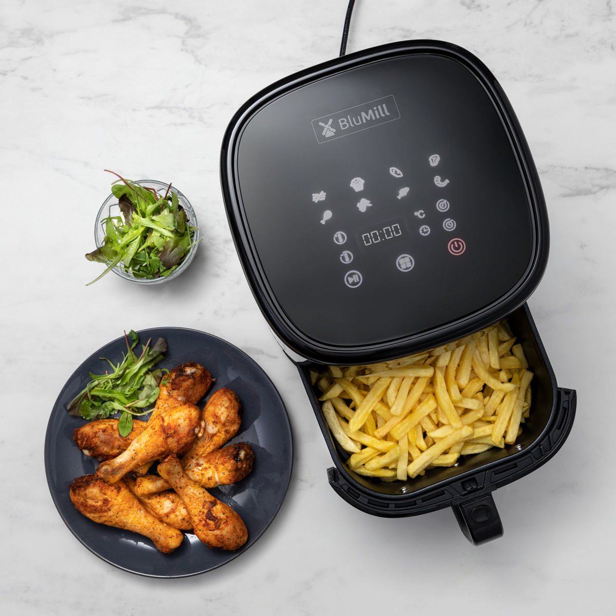 Zwarte airfryer met friet, kip en salade.
