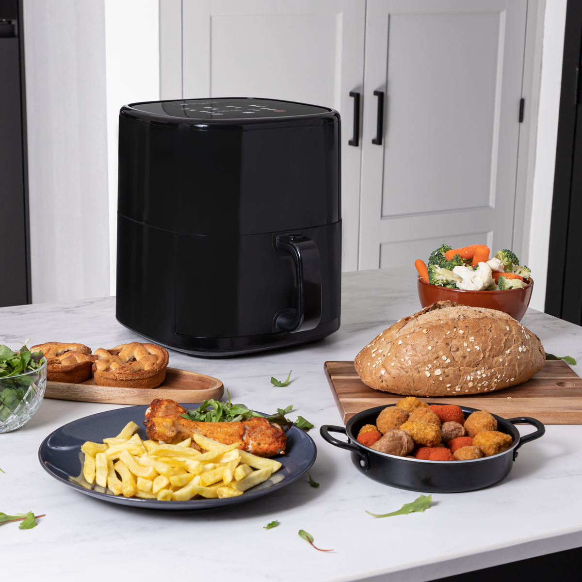 Zwarte airfryer met etenswaren zoals friet, kip, brood en groenten op marmer.